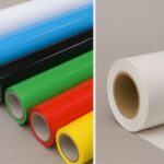 Comparación visual entre vinil de corte en colores sólidos (blanco, azul, negro, verde, rojo y amarillo) y un rollo de vinil blanco para impresión desplegado sobre fondo gris.