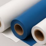 Tres rollos de lona, dos de color blanco y uno azul, enrollados sobre tubos de cartón y dispuestos sobre una superficie gris.
